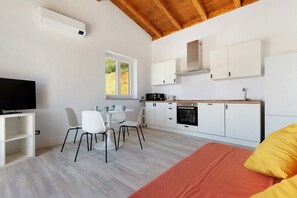 Een moderne keuken met witte kastjes, een eethoek met een tafel en stoelen, een televisie en een groot raam.