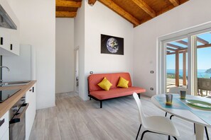 Una cucina moderna con mobili bianchi e un piano di lavoro in legno, un divano rosso con cuscini gialli e un tavolo da pranzo con sedie.