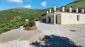 Une maison avec une allée en gravier, une construction à un seul étage et une vue sur une colline verdoyante.