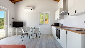 Une cuisine moderne avec des armoires blanches, un plan de travail en bois et un four encastré. On y trouve un coin repas avec une table et des chaises, ainsi qu’un téléviseur fixé au mur.