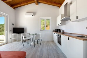 Una cucina moderna con mobili bianchi, un piano di lavoro in legno e un forno integrato. C'è un'area pranzo con tavolo e sedie, e un televisore fissato al muro.