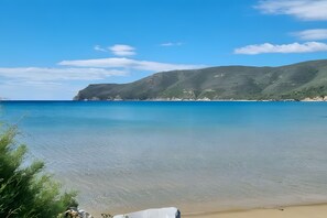 A beach with clear water, a sandy shore, and green hills in the background.