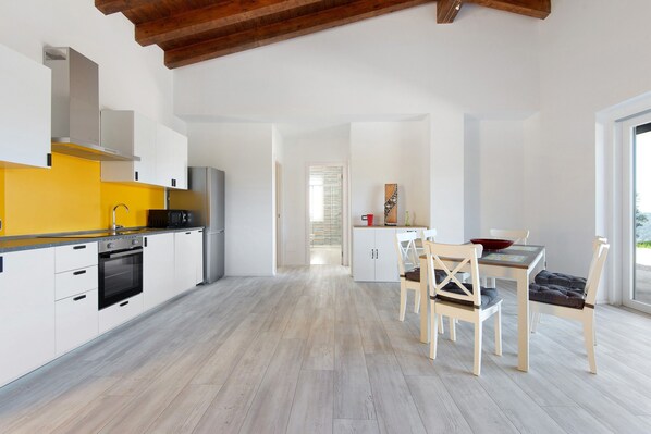 A modern kitchen with white cabinets, a yellow countertop, and a dining area with wooden chairs and a table.