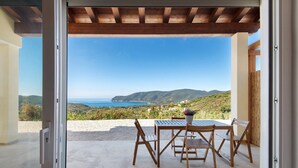 An open door to a patio with a table and chairs, overlooking a scenic landscape with hills and a body of water. - Adriana Trilocale Apartment with Sea View and Wi-Fi (Lacona)