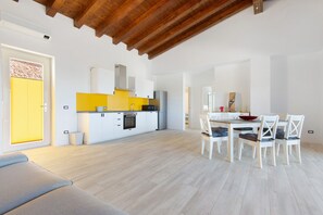 Una cucina moderna con mobili bianchi, un piano di lavoro giallo e un'area pranzo con sedie bianche e un tavolo in legno.
