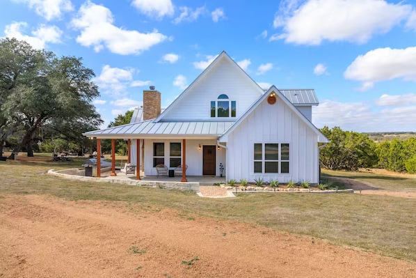 A white two-story house with a covered porch, a chimney, and a view of the surrounding landscape.