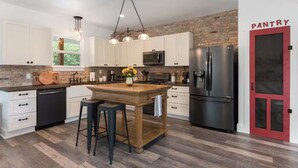 Een moderne keuken met witte kastjes, een houten eiland, een roestvrijstalen koelkast en een rode pantrydeur.