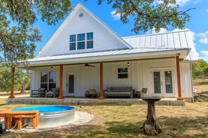 A white house with a covered porch, a swimming pool, and a tree in the foreground.