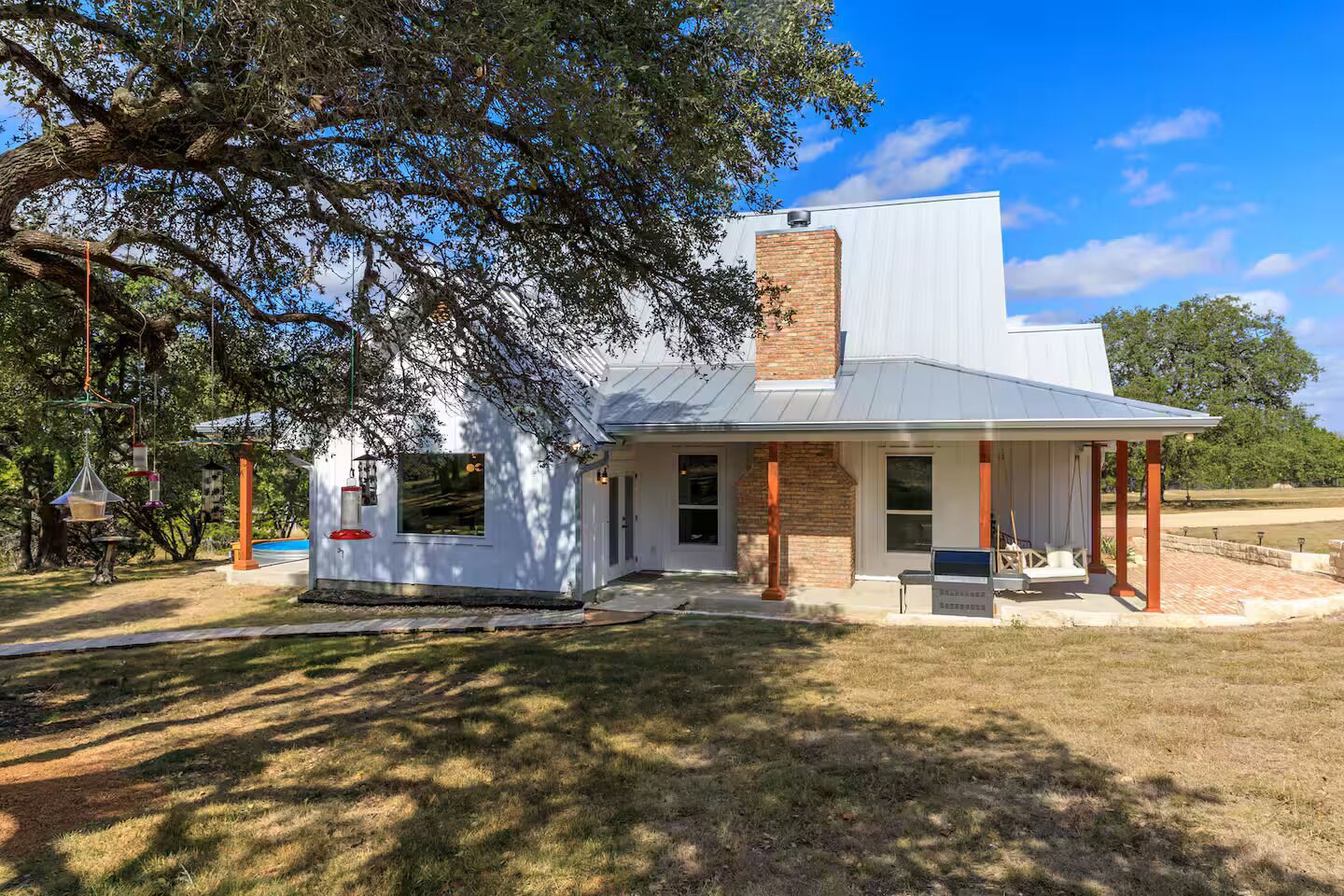 A single-story house with a white exterior, a brick chimney, and a covered porch.