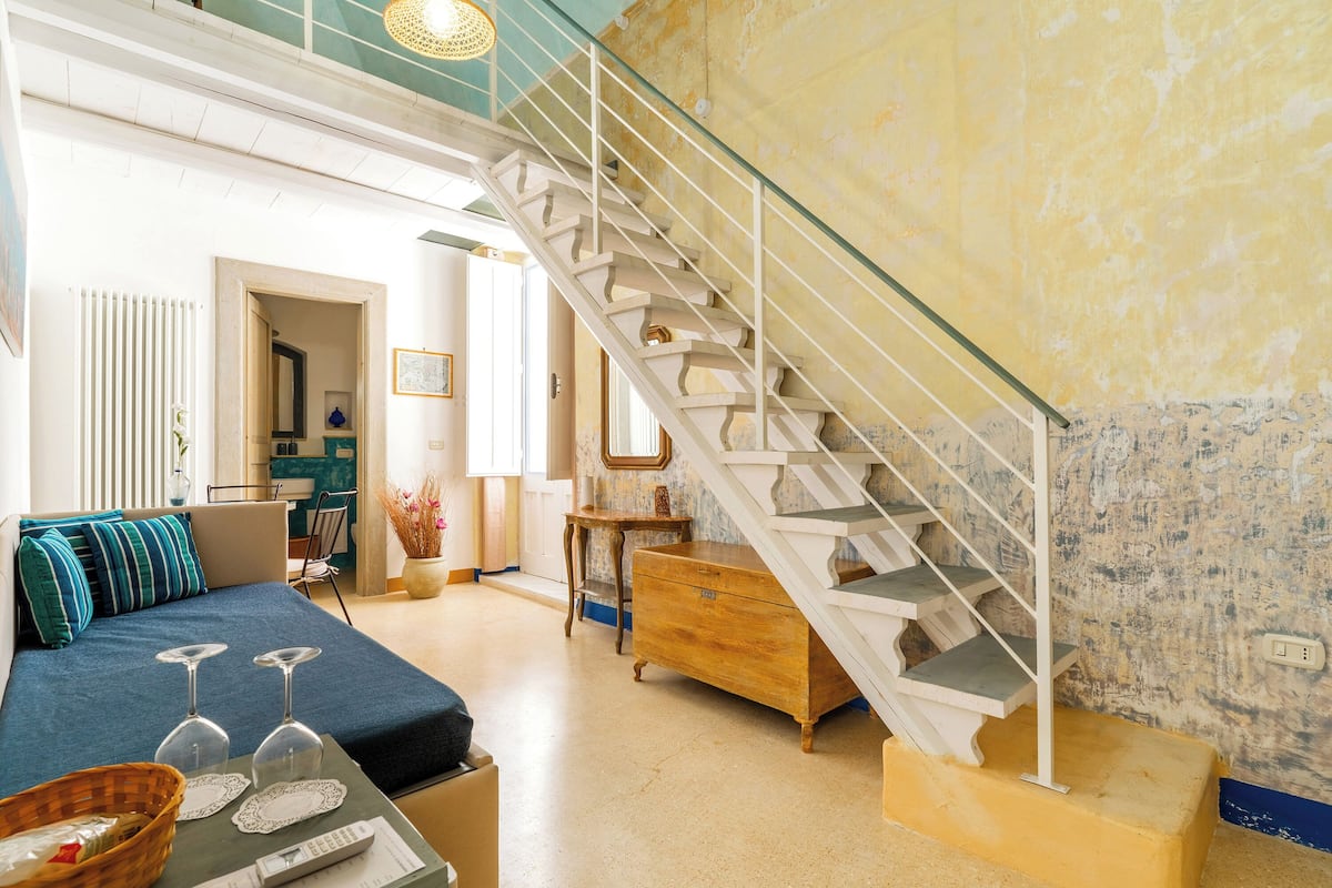 A spacious living area with a staircase, a sofa, a coffee table with wine glasses, and a wooden cabinet.