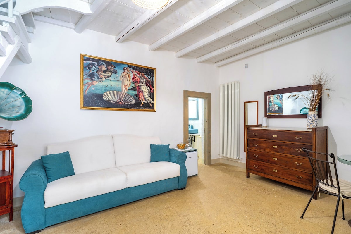A room with a white sofa, a wooden dresser, a chair, and a painting on the wall.