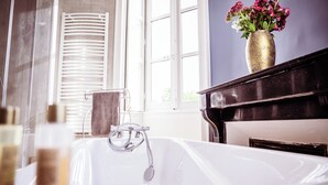 Une salle de bain avec une baignoire, un porte-serviettes et un vase rempli de fleurs posé sur un piano.