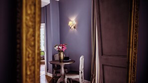 Une pièce avec un mur de couleur violet foncé, une table ronde ornée d’un vase de fleurs, une chaise et un luminaire fixé au mur.