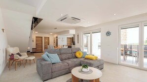 Een moderne woonkamer met een grijze modulaire bank, een ronde salontafel en een eetgedeelte met een glazen deur die naar buiten leidt.