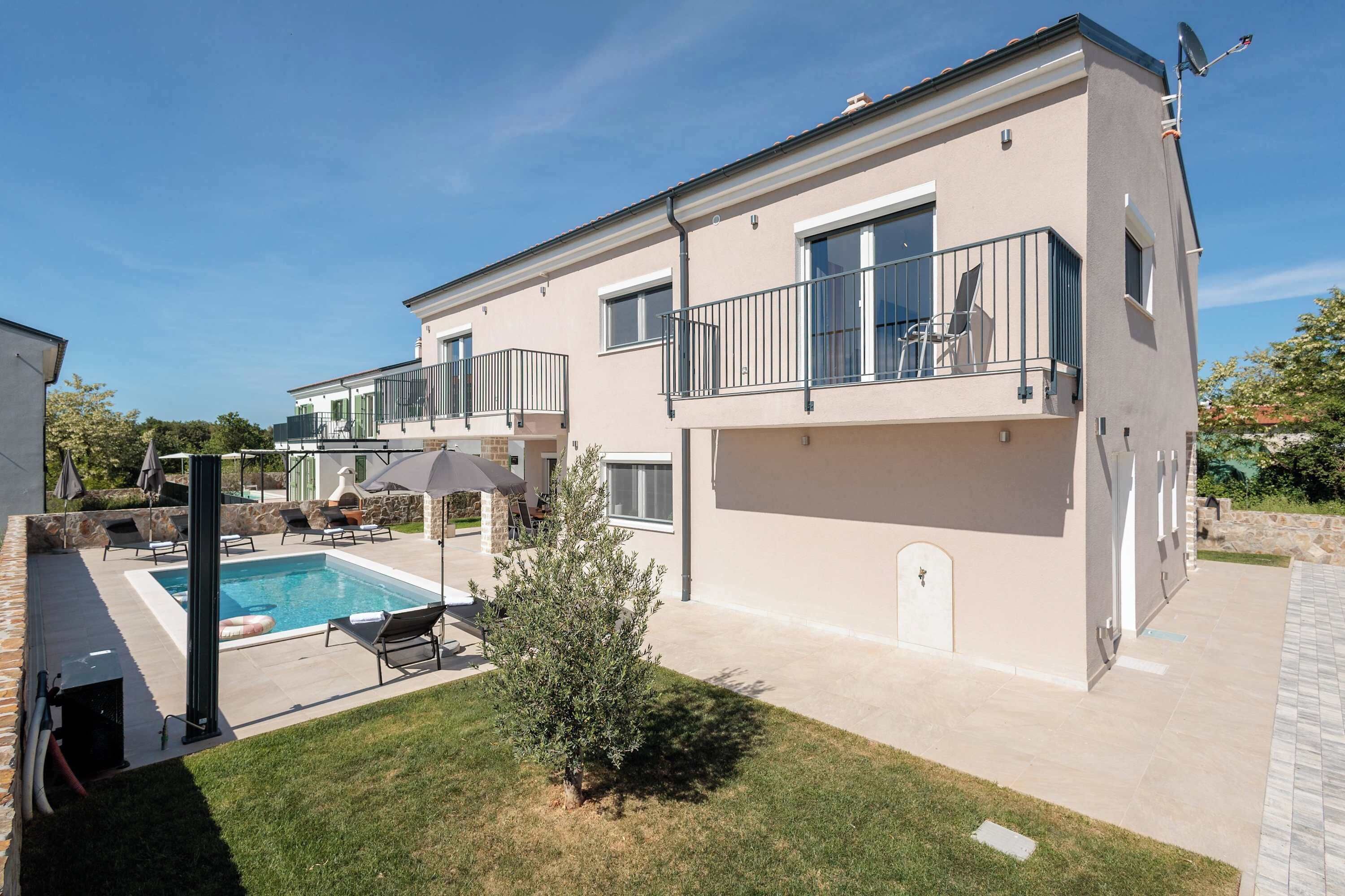 A two-story house with a swimming pool, outdoor seating, and a small garden.