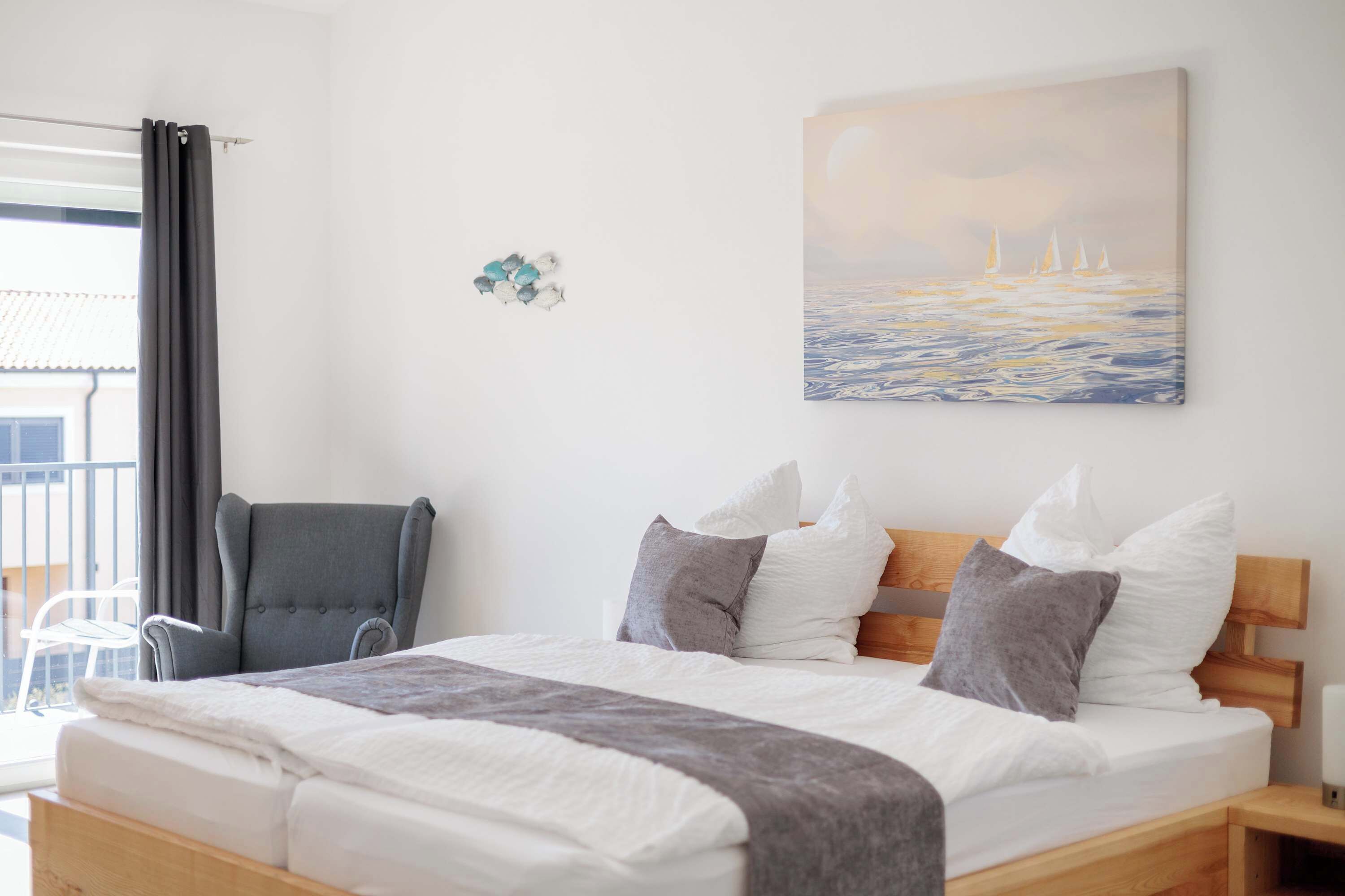 Ein Schlafzimmer mit Bett, Kissen, einem Sessel, einem Gemälde und einem Balkon.