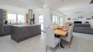 Een moderne keuken met een centraal eiland, een eetgedeelte met stoelen en een grijze bank.