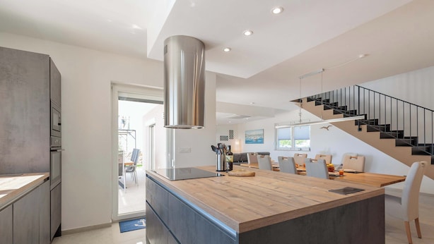 Een moderne keuken met een centraal eiland, een roestvrijstalen afzuigkap en een trap naar een hoger niveau.