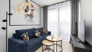 A modern living room with a dark blue sofa, two round tables, a mounted TV, and a large abstract painting of a guitar. - Air Condtioned Apartment | Rooftop Pool (Mielno)