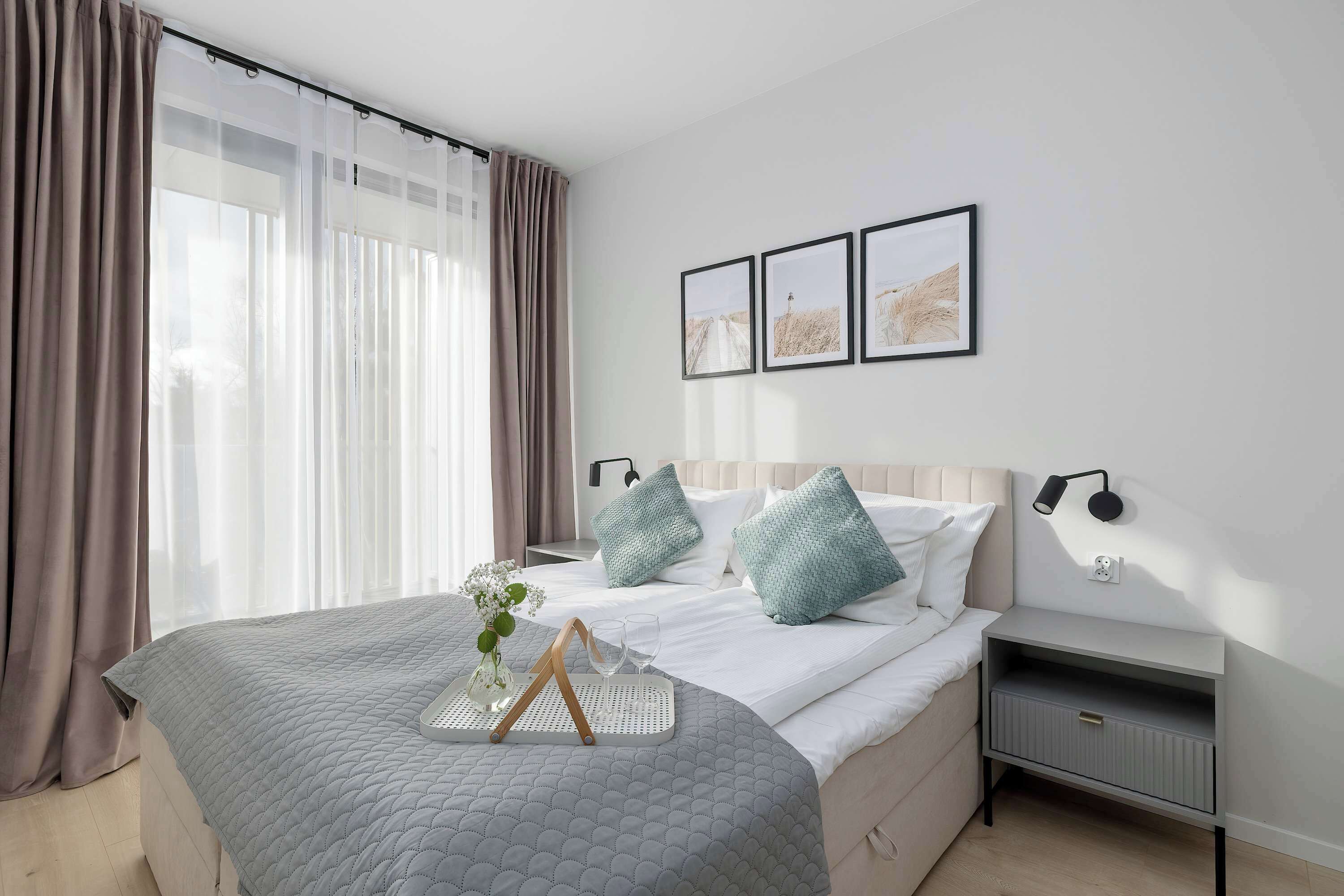 A hotel room with a bed, bedside tables, a nightstand, and a window with curtains.