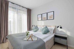 Hotellihuone, jossa on sänky, yöpöydät, yölamppu ja ikkuna, jossa on verhot.