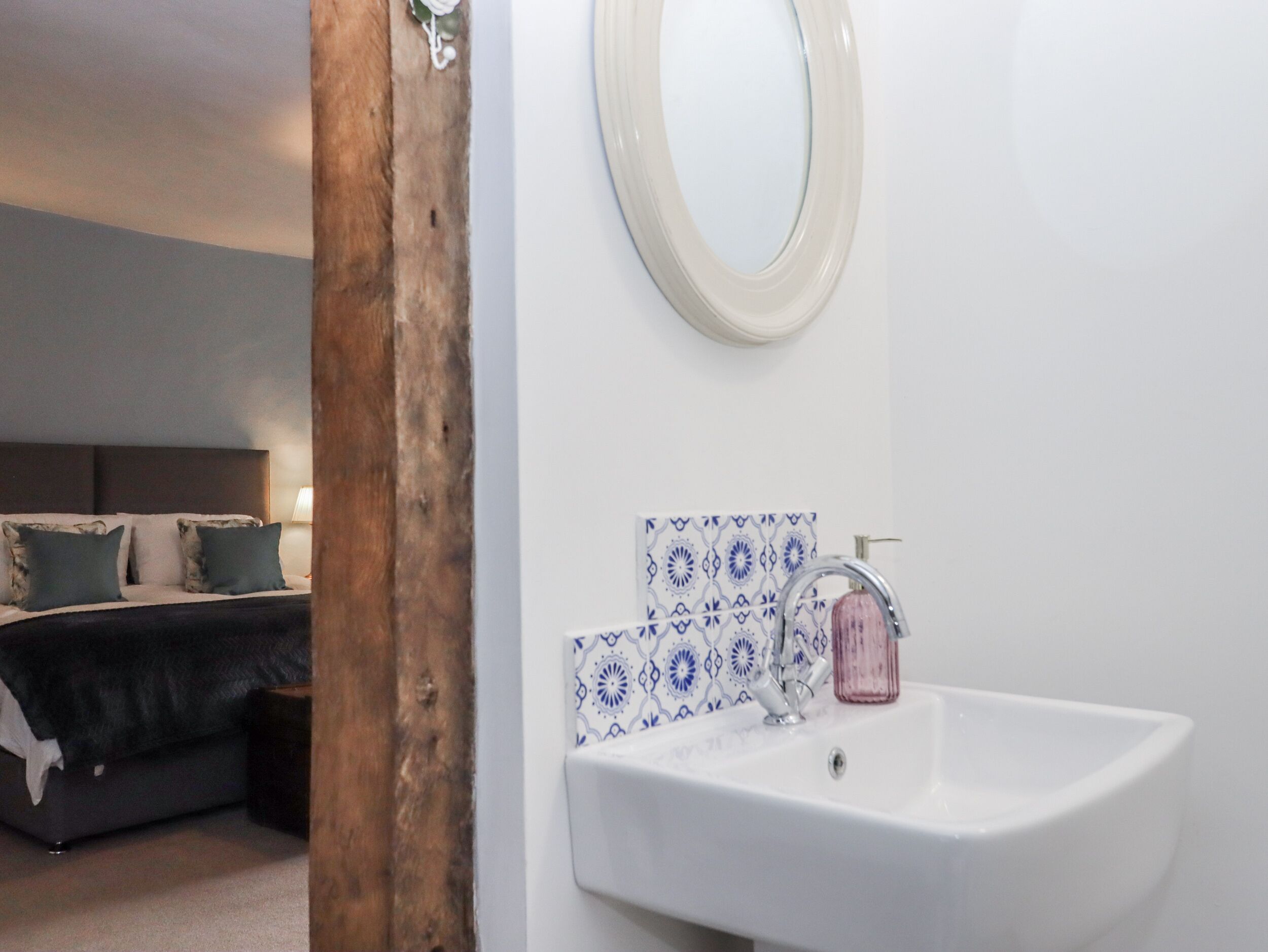 A bedroom with a bed, a bedside table, a nightstand, and a wall-mounted mirror.