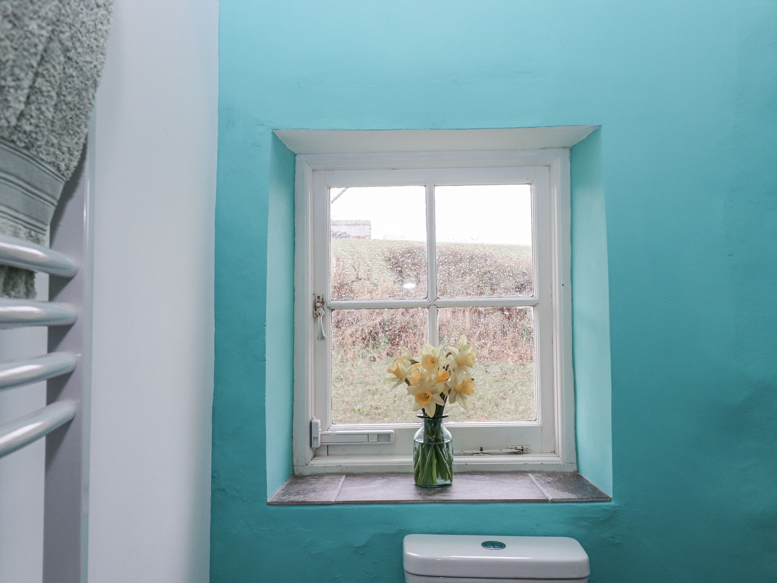 A bathroom with a window, a white toilet, and a vase with flowers.