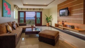 A modern living room with a sofa, ottoman, coffee table, TV, and a balcony with a view.