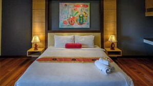 A hotel room with a large bed, two bedside lamps, a colorful painting above the bed, and a wooden floor.