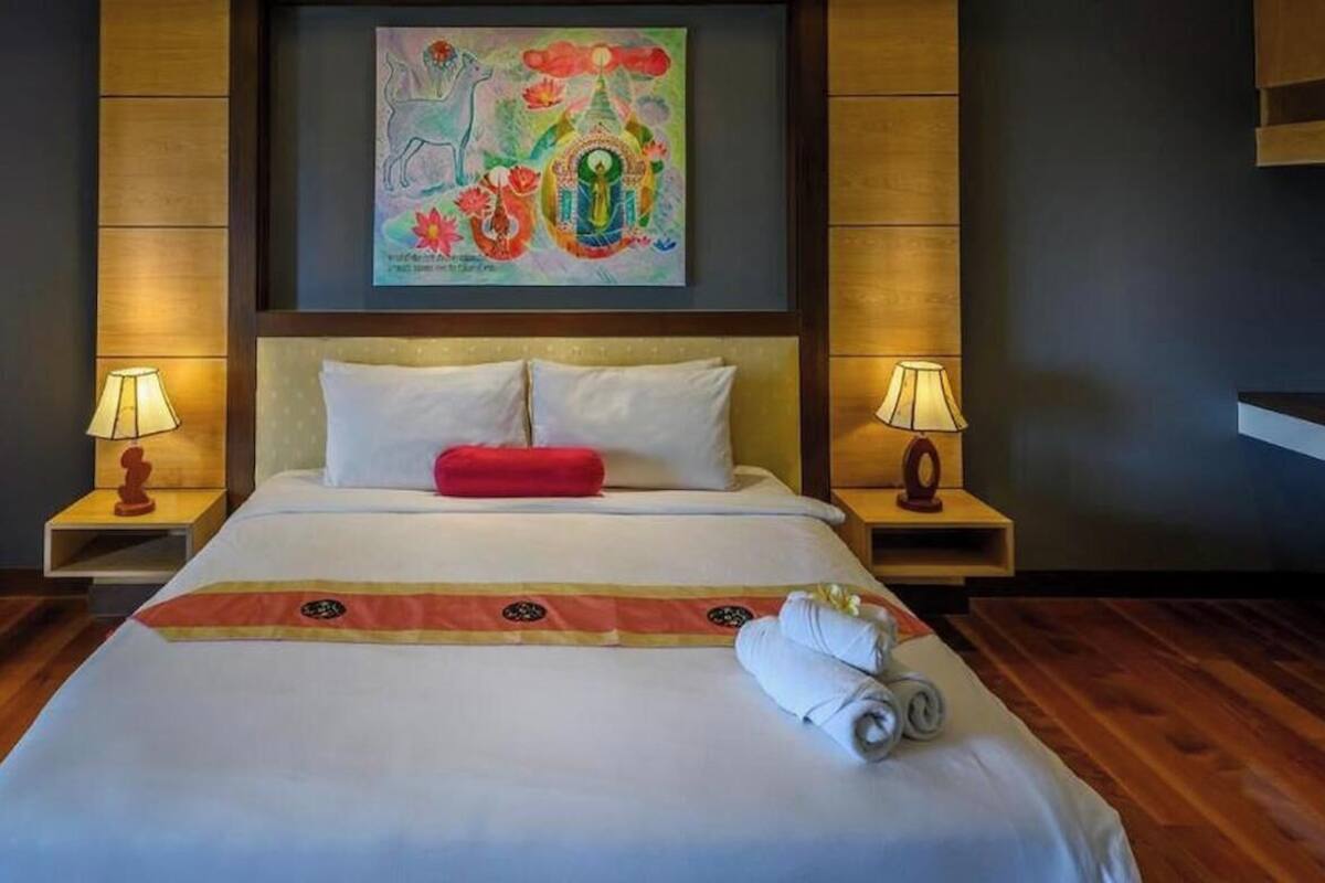 A hotel room with a large bed, two bedside lamps, a colorful painting above the bed, and a wooden floor.