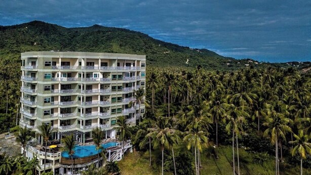 A multi-story hotel with balconies, a swimming pool, and surrounded by palm trees.