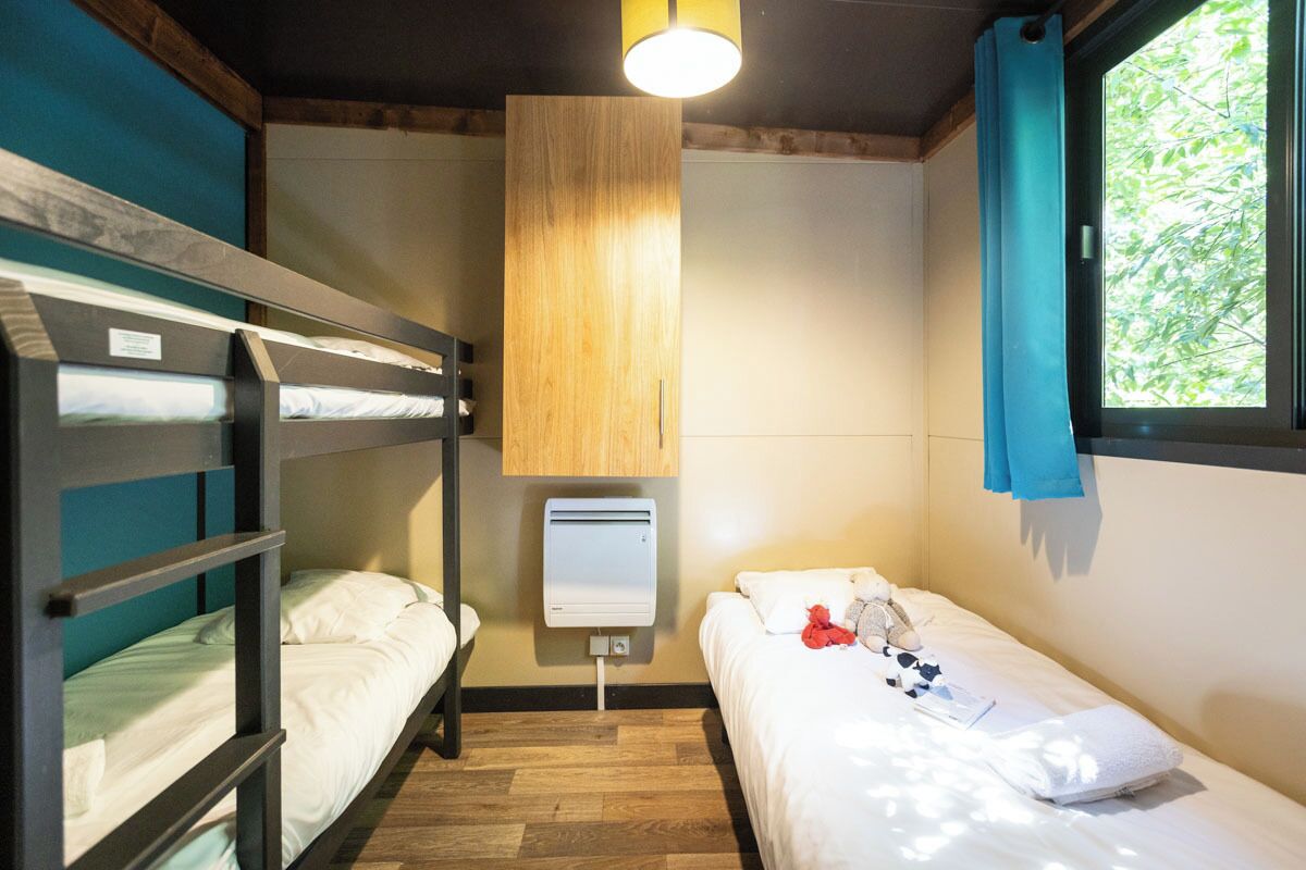 A room with bunk beds, a bedside heater, a window with curtains, and a view of greenery outside.