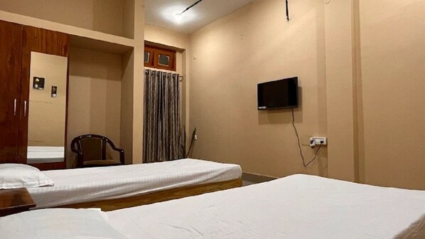 A hotel room with two beds, a wooden wardrobe, a chair, a television, and a curtain.