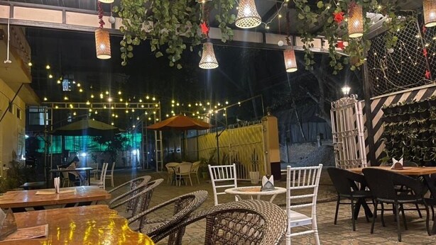 An outdoor dining area with wicker furniture, string lights, and hanging plants. - Palaash Bon Homestay (Guwahati)