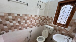 A bathroom with a toilet, sink, shower, and a window with a metal grid. - Palaash Bon Homestay (Guwahati)