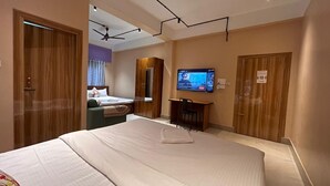 A hotel room with a large bed, a desk, a television, and a wardrobe. - Palaash Bon Homestay (Guwahati)