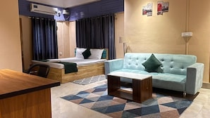 A hotel room with a bed, a light blue sofa, a wooden desk, and a patterned rug. - Palaash Bon Homestay (Guwahati)
