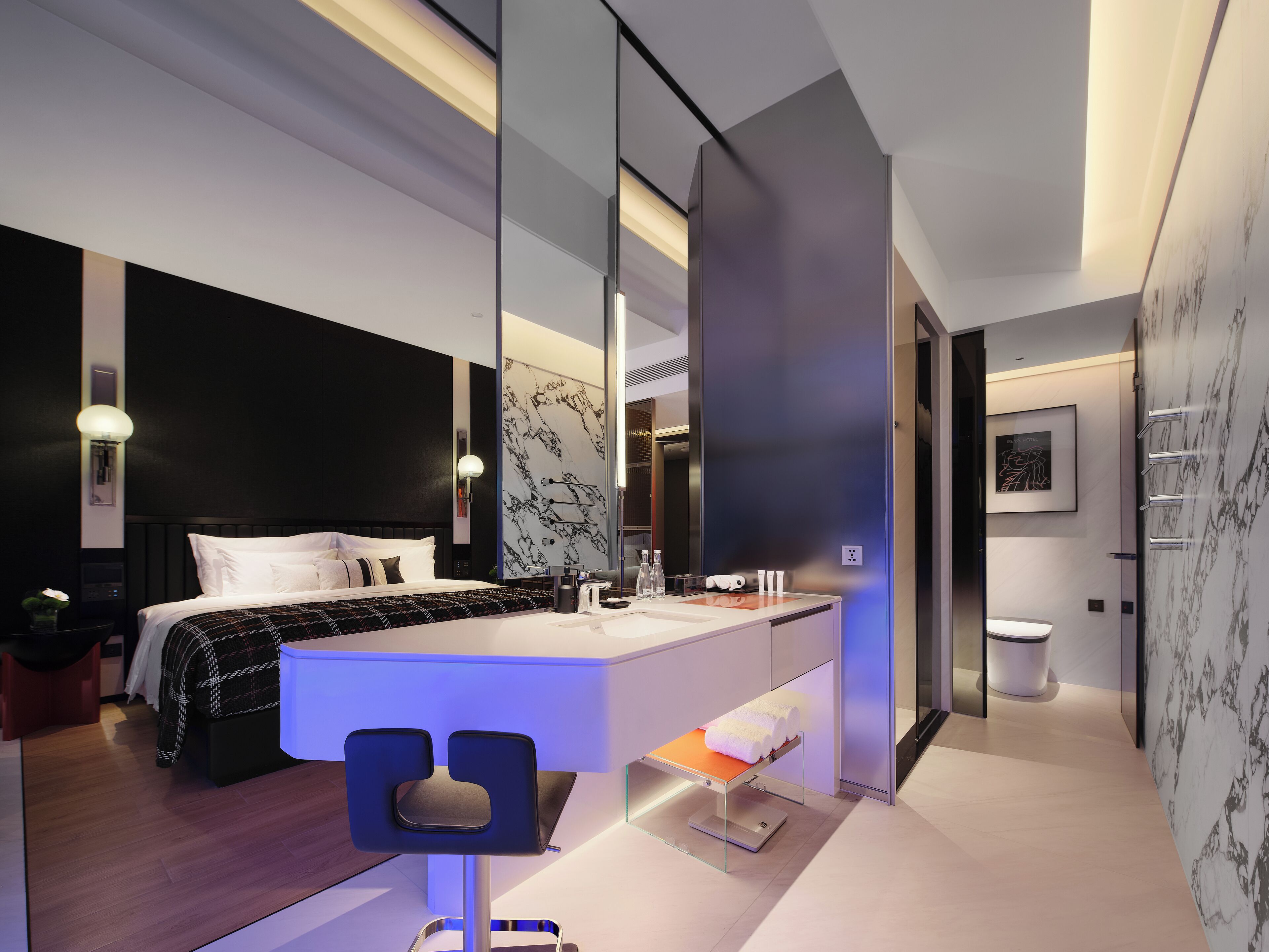A modern hotel room with a large bed, a bathroom with a marble wall, and a small seating area.