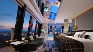Une chambre d’hôtel moderne avec vue sur la ville, un grand lit, un canapé, un coin repas et une cuisine.