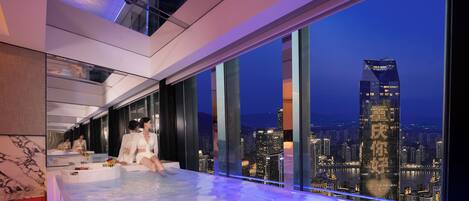Habitación de hotel moderna con vista a la ciudad, un ventanal grande y un área de descanso junto a la ventana.