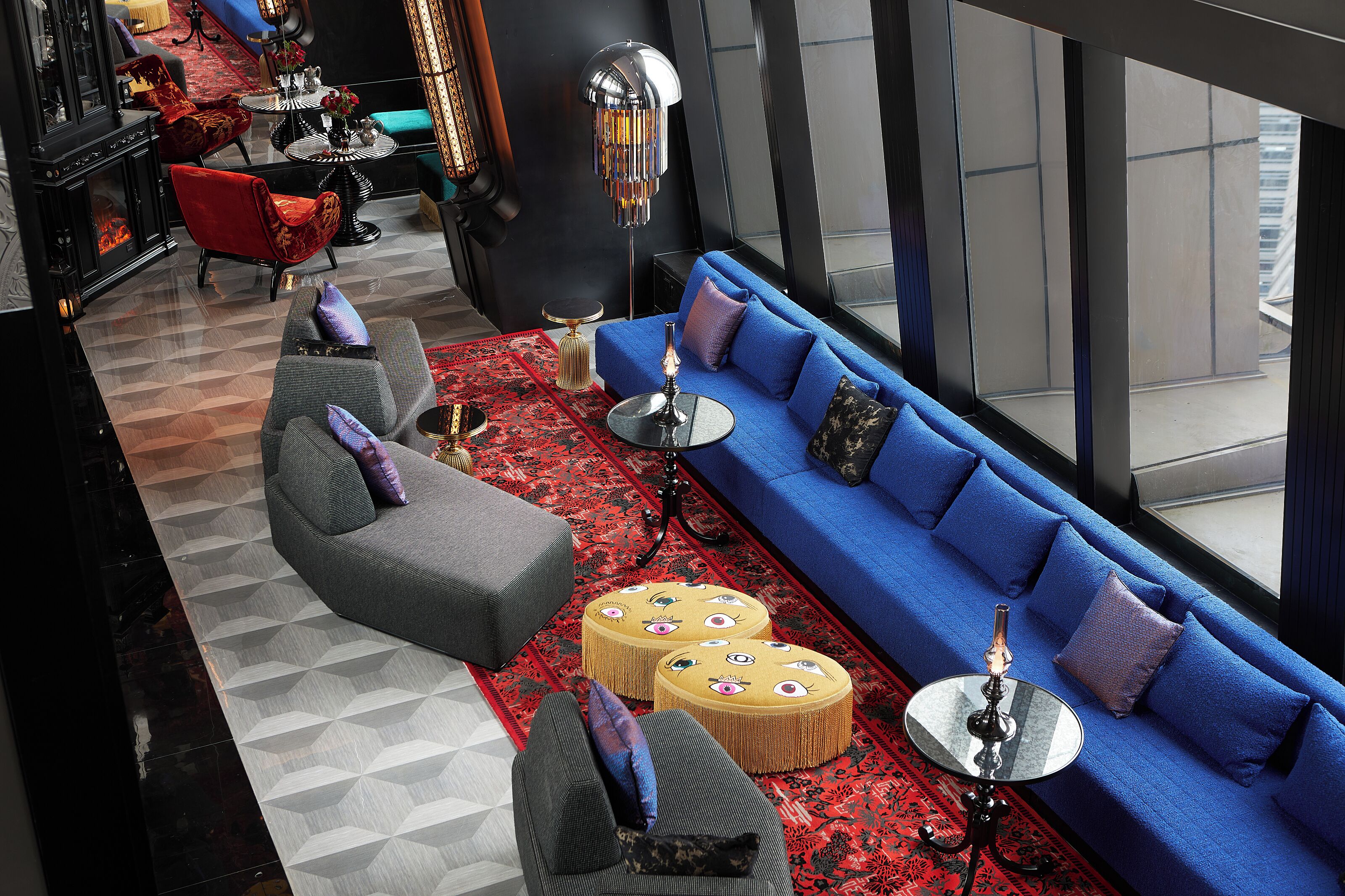 A modern lounge with a blue sofa, red armchairs, and a patterned rug.