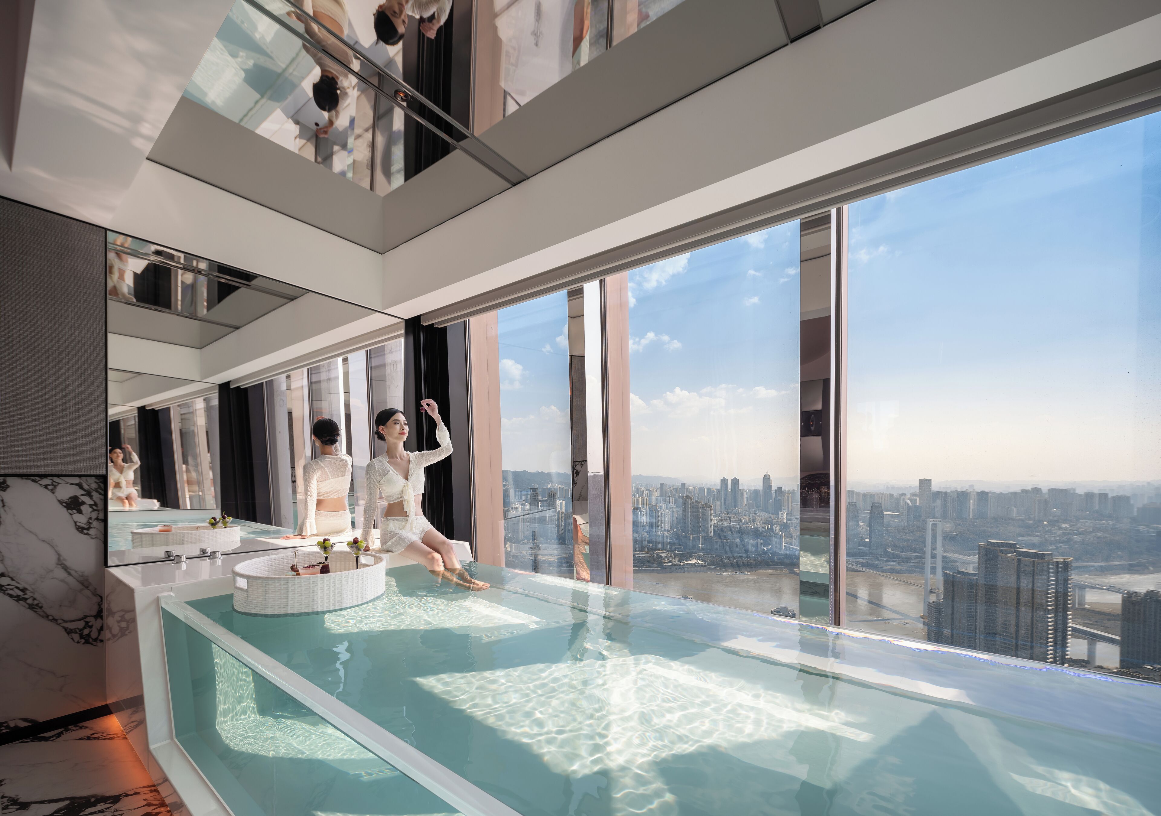 Un intérieur moderne avec une piscine à débordement en verre, de grandes fenêtres et une vue sur la ville.