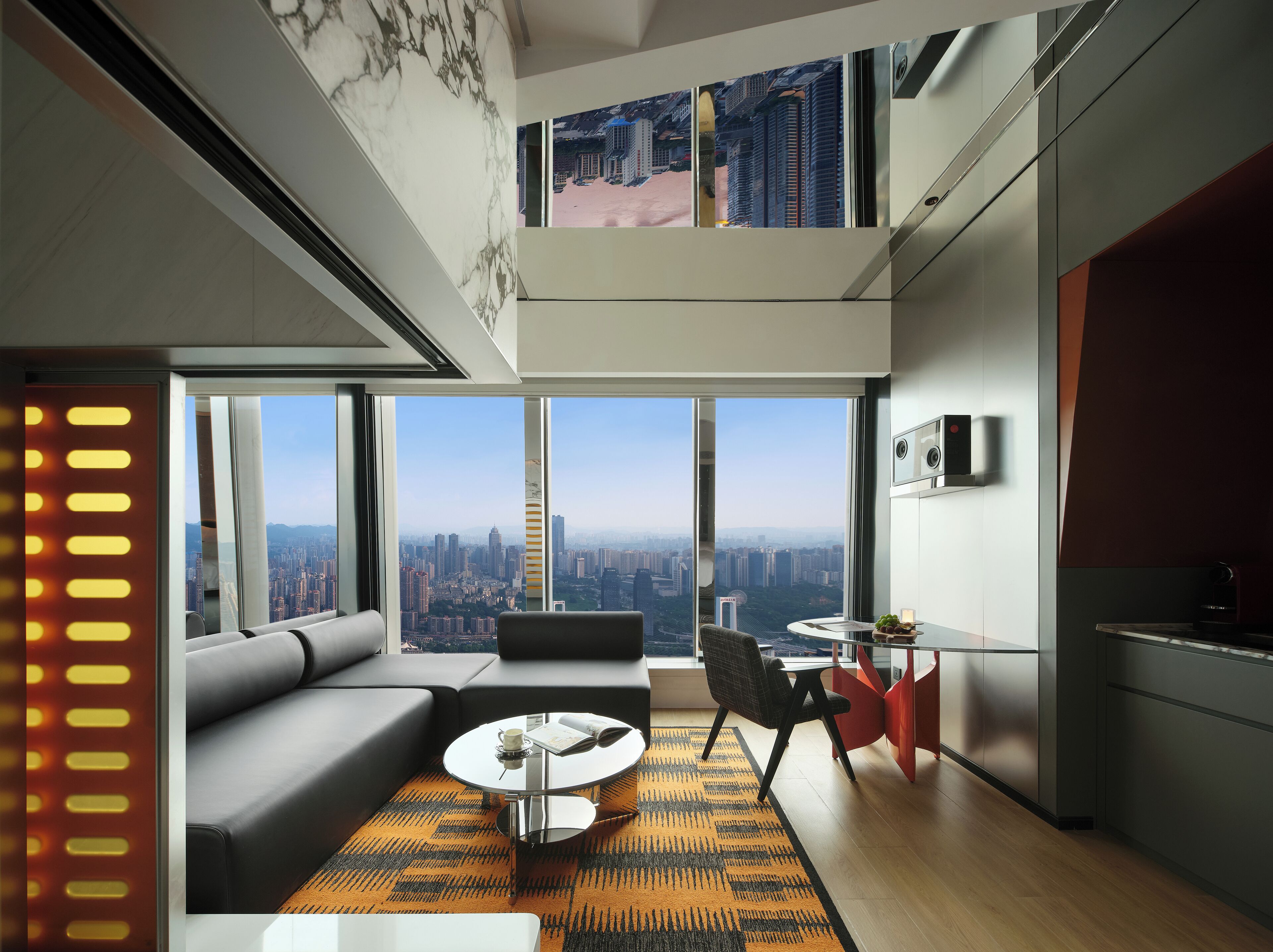 Un salón moderno con sofá, mesa de centro y comedor, con amplias ventanas y vista a la ciudad.