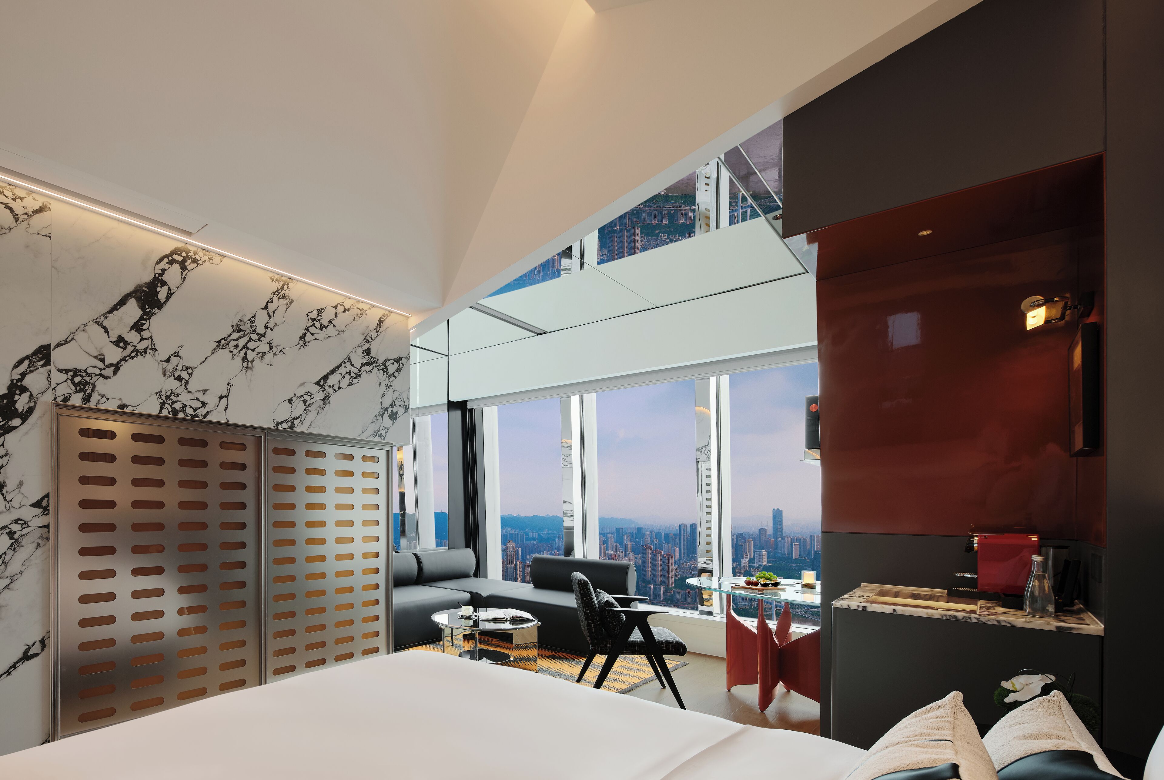 Une chambre d’hôtel moderne dotée d’un grand lit, d’un canapé, d’une table à manger et offrant une vue sur le paysage urbain.