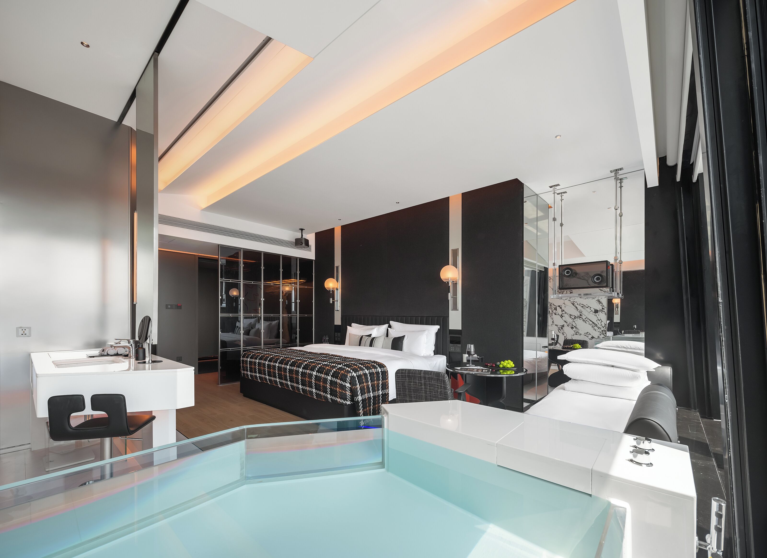 A modern hotel room with a large bed, a glass-enclosed walk-in closet, a separate bathroom, and a pool area.