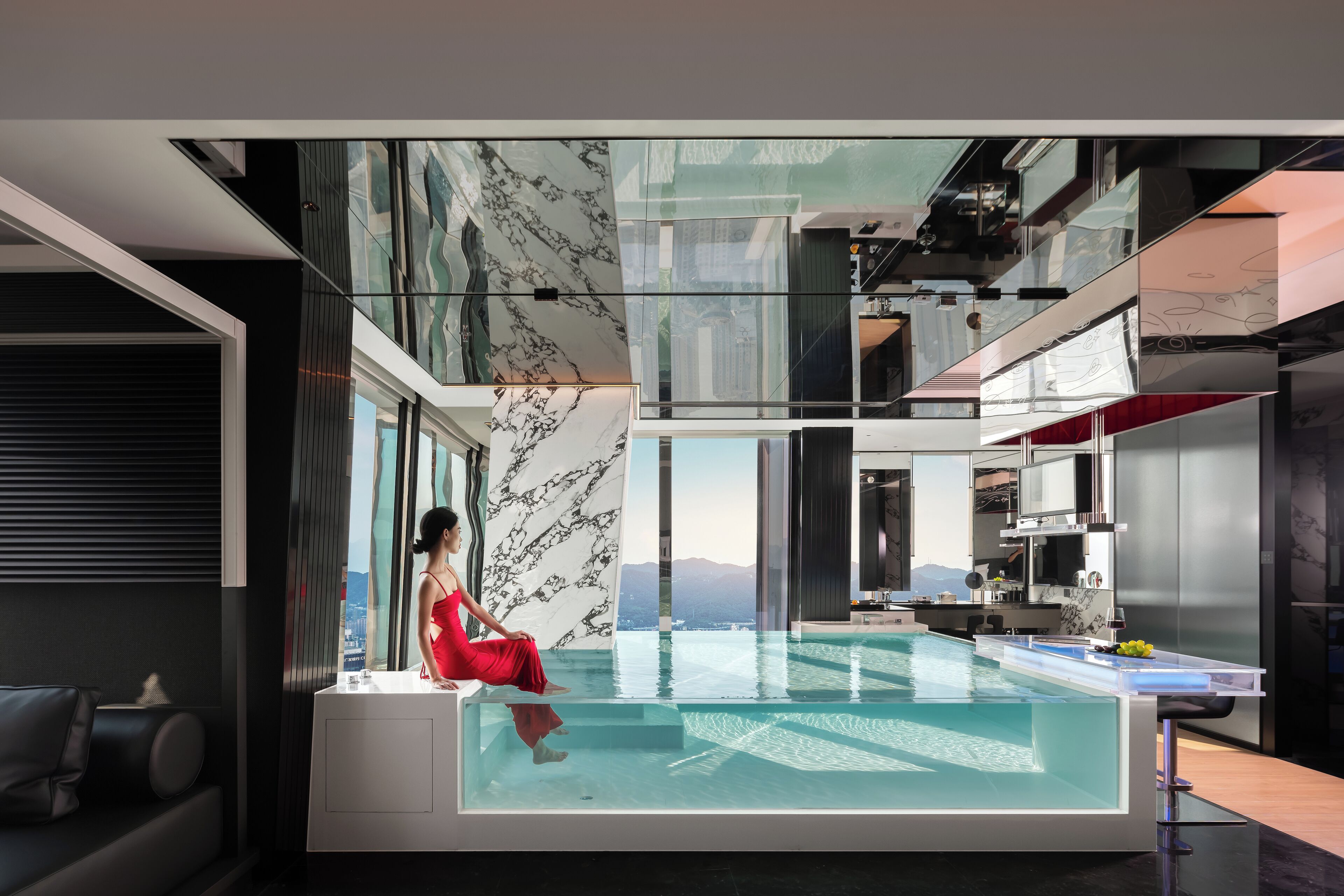 A modern interior with a large glass pool, a woman in a red dress, and a city view.