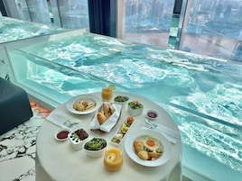 Una mesa de comedor con alimentos para el desayuno y una mesa de vidrio con vista a un paisaje urbano.