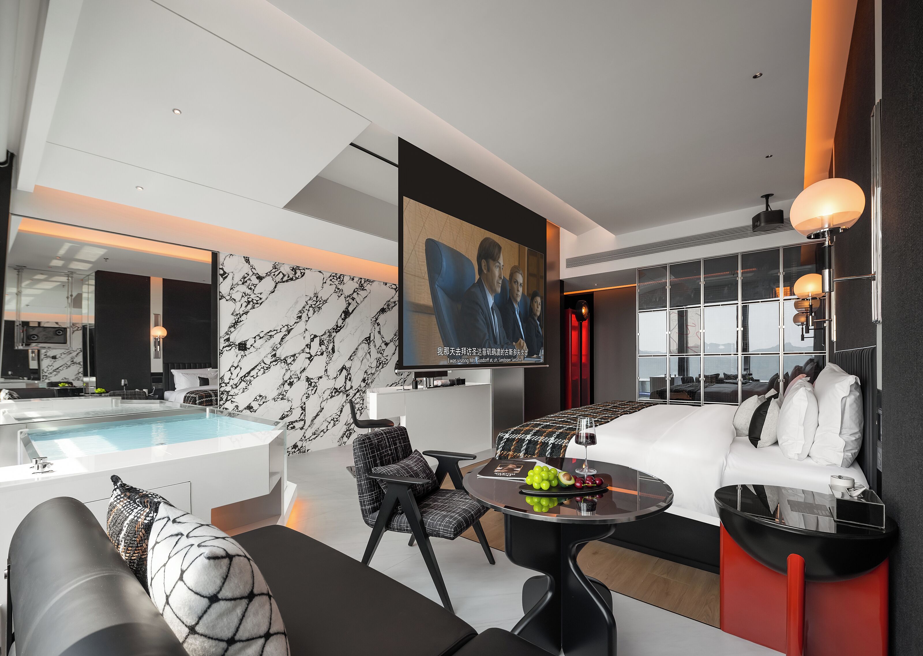 A modern hotel room with a large bed, a seating area with a table, a TV, a large window, and a pool area.