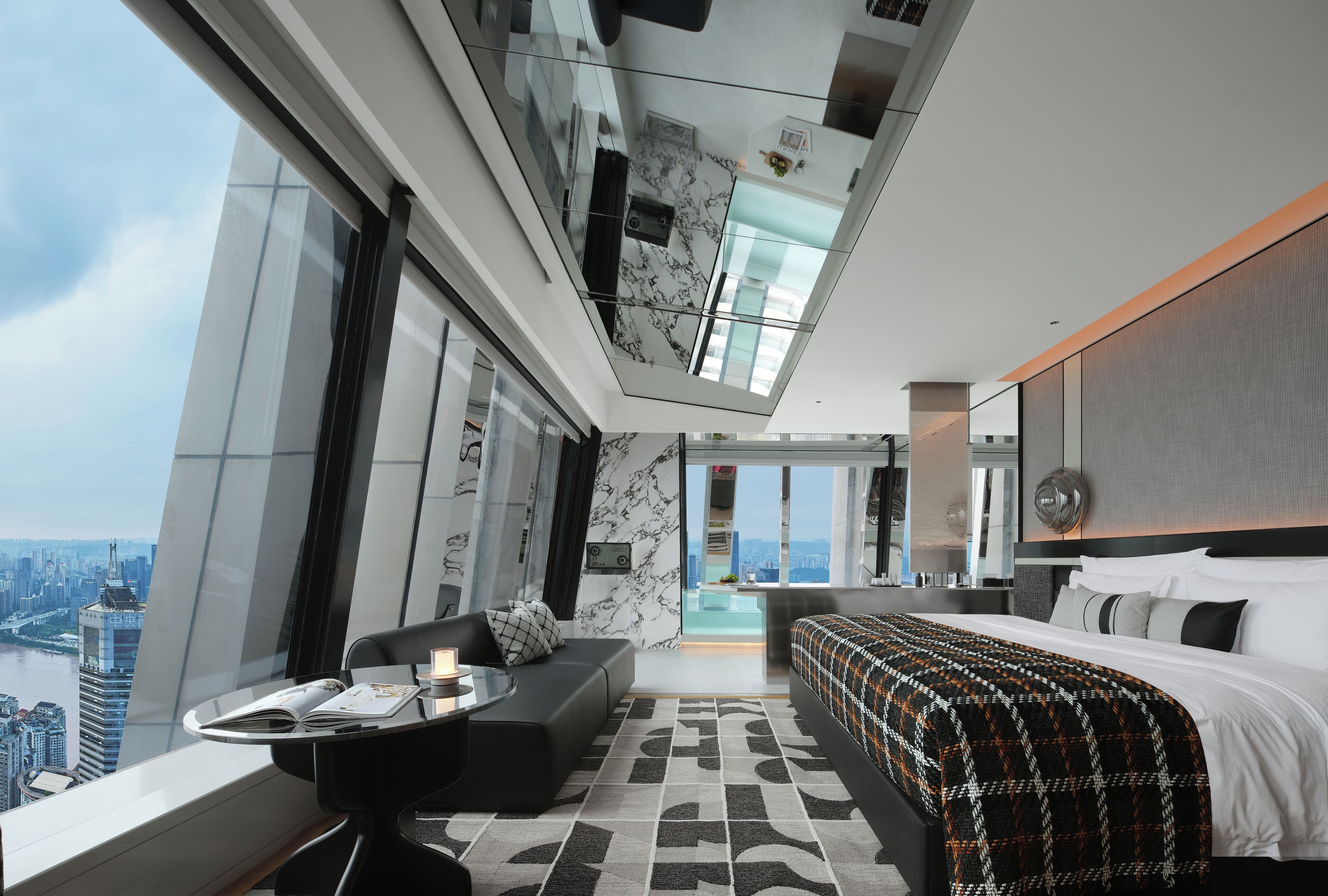 Moderni hotellihuone, jossa on suuri ikkuna, sänky, sohva, pieni pöytä ja näkymä kaupunkiin.