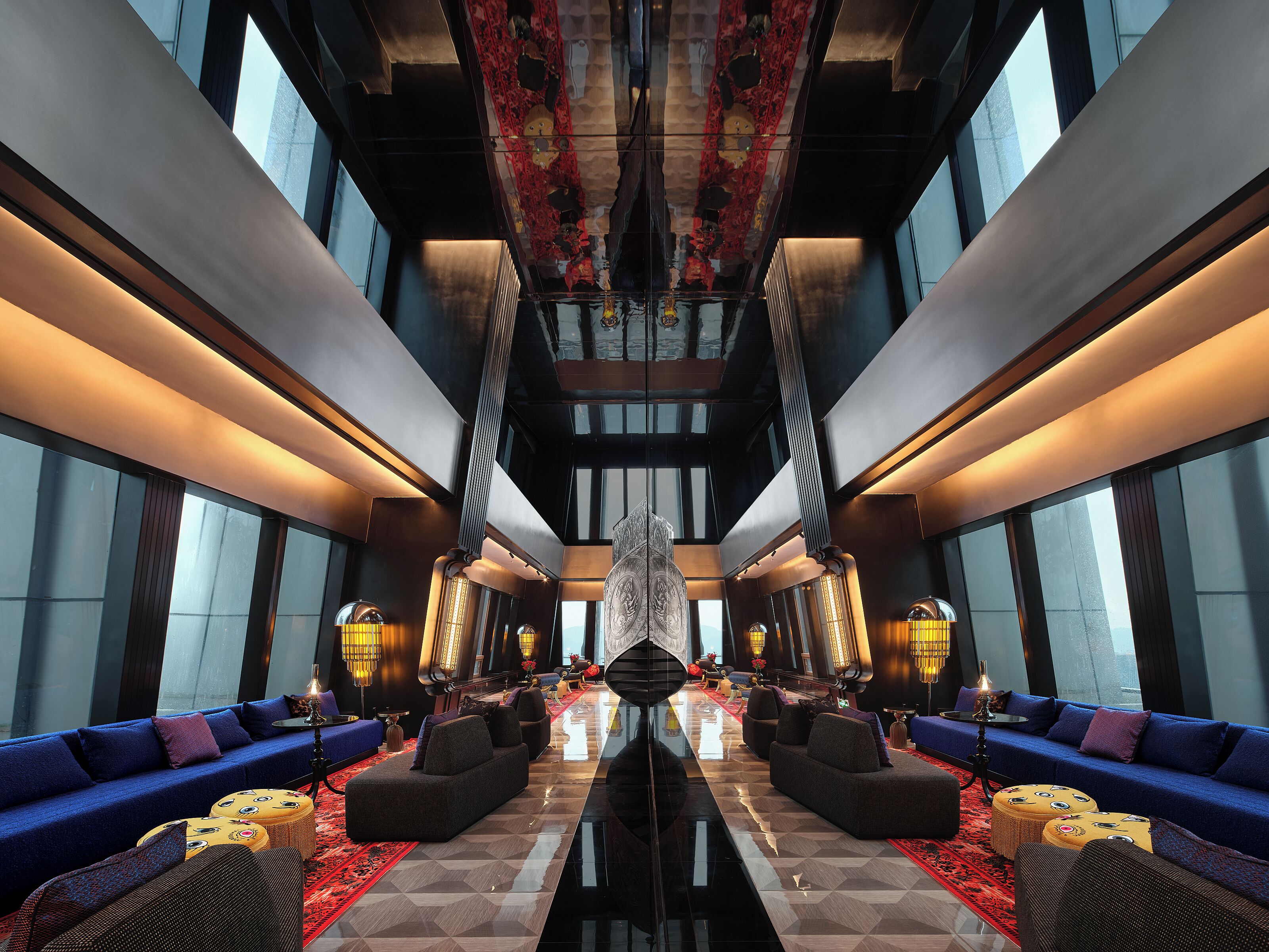 A spacious lobby with a central chandelier, sofas, and a patterned floor.